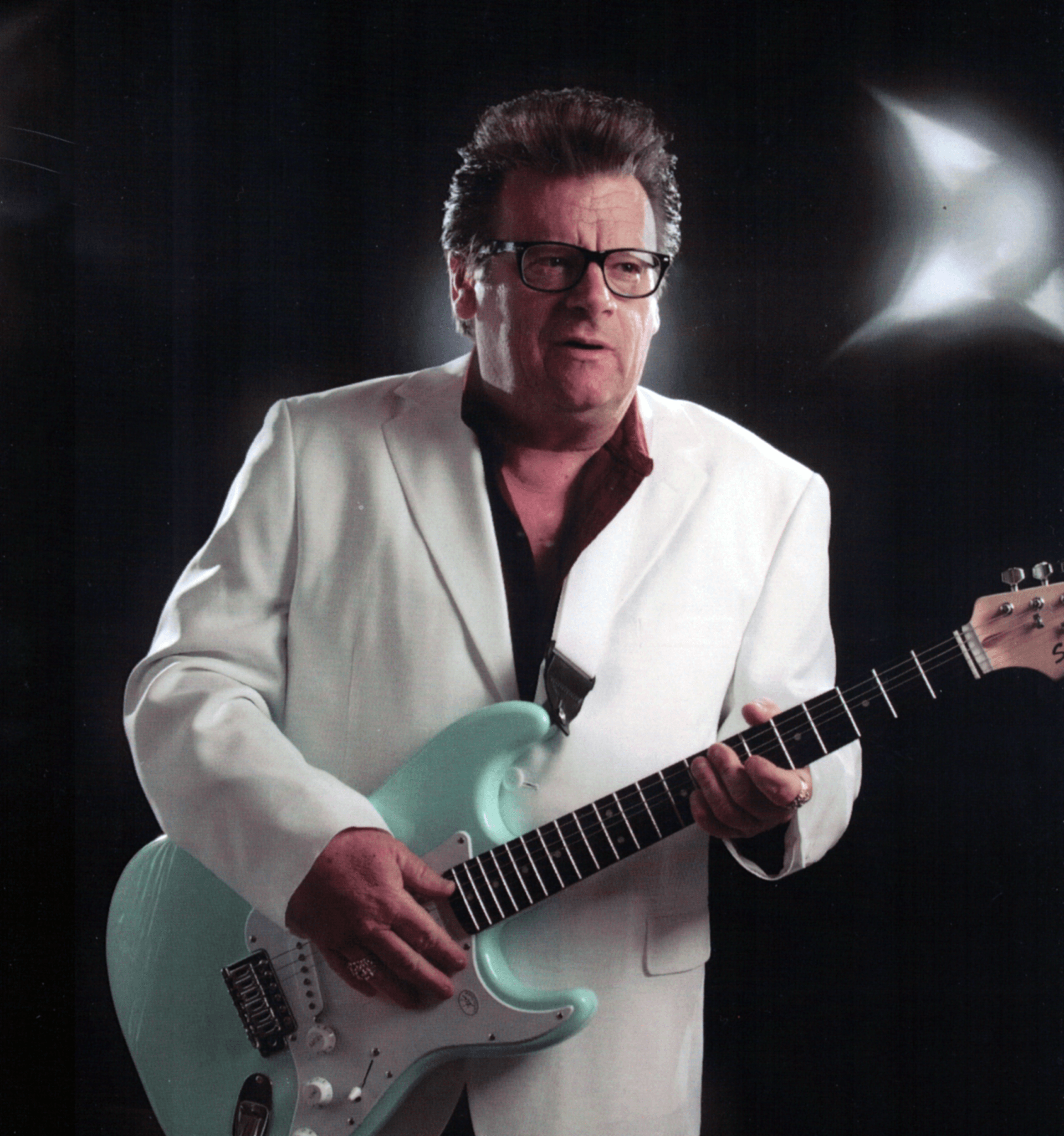 Musician in white jacket playing a mint-green electric guitar against a dark background