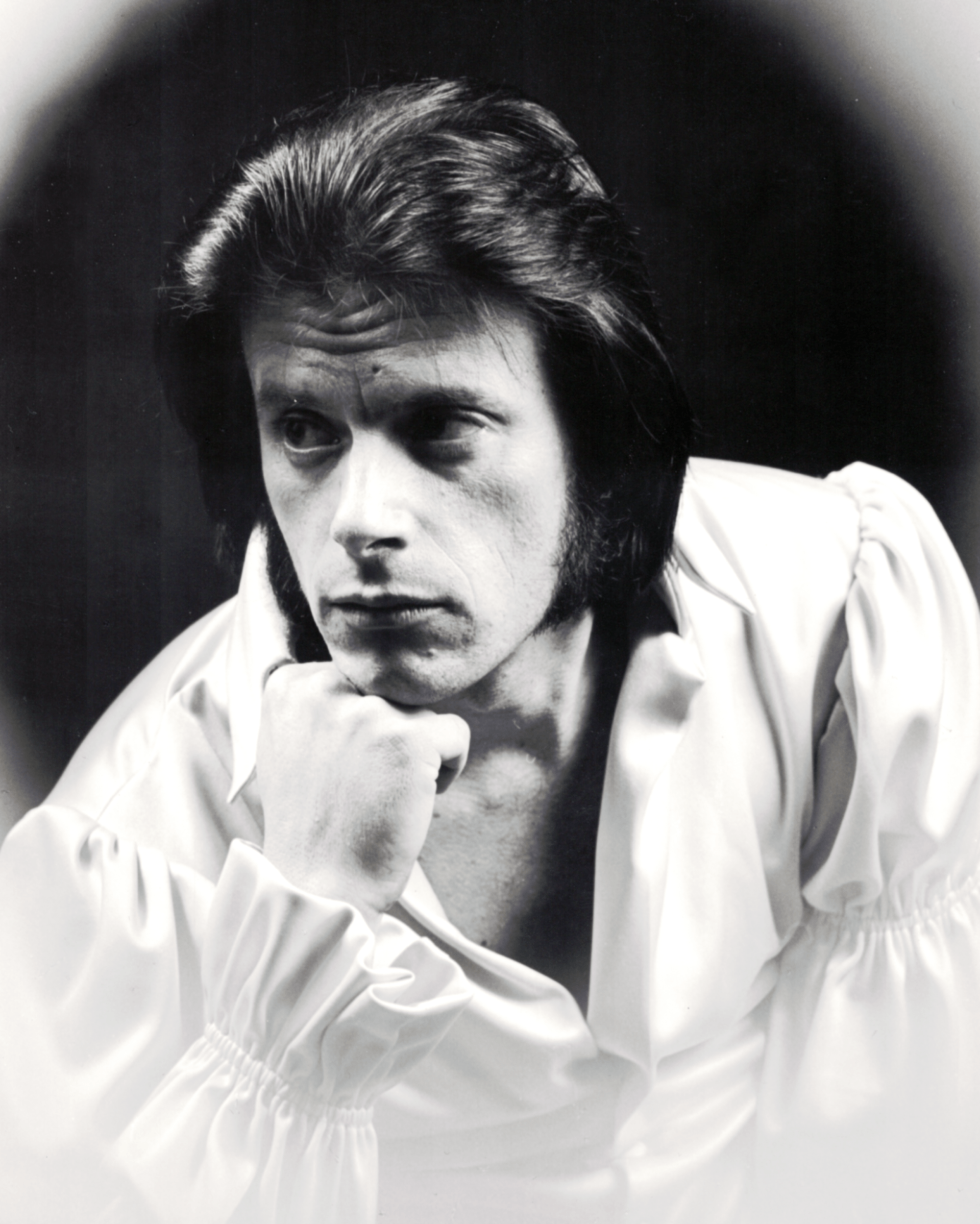 Black-and-white portrait of a pensive man resting his chin on his hand, wearing a white shirt.